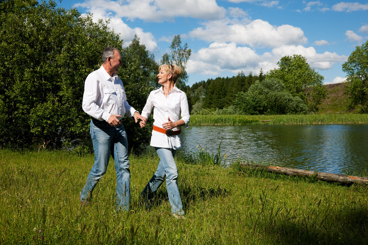 Early retiree couple walking in long grass near water on a sunny day